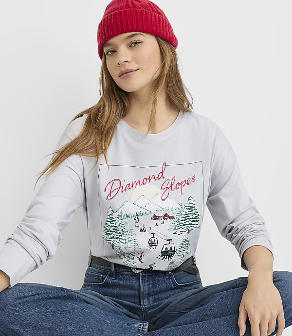 A woman wearing a red beanie and a graphic long-sleeve shirt sits against a plain white background.