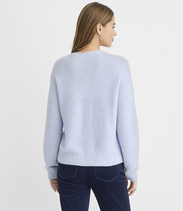A woman wearing a light blue fuzzy sweater and dark blue corduroy pants stands against a plain white background.