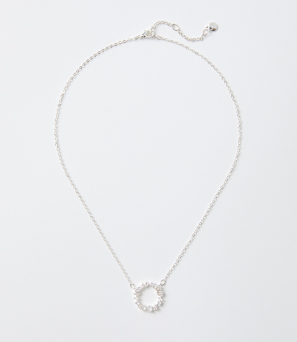 A silver necklace with a circular sparkling pendant rests on a plain white background.