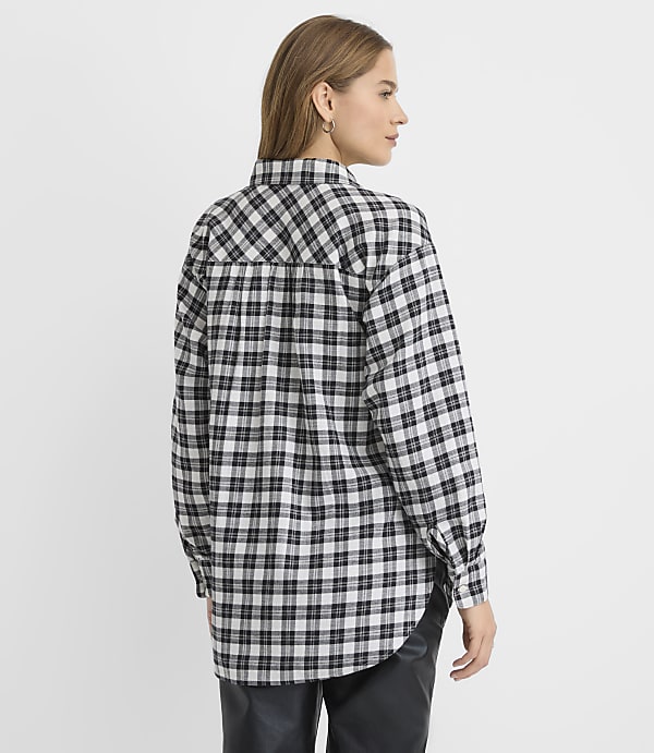 A woman wearing a black and white plaid shirt and black leather pants stands against a plain white background.