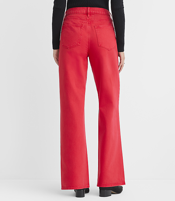 A person wearing bright red wide-leg jeans and black boots stands against a plain white background.
