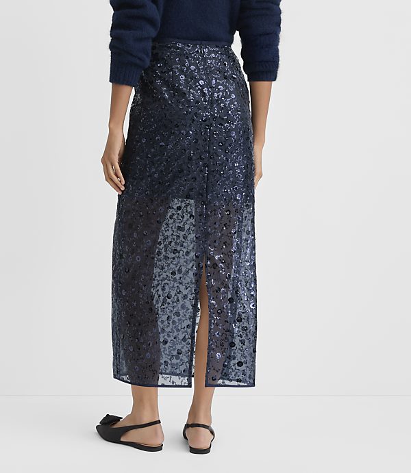 A person wearing a navy blue sequined skirt and a fuzzy sweater stands against a plain white background.