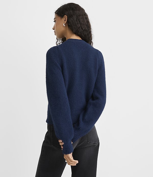 A woman wearing a navy blue fuzzy sweater and black jeans stands against a plain white background.