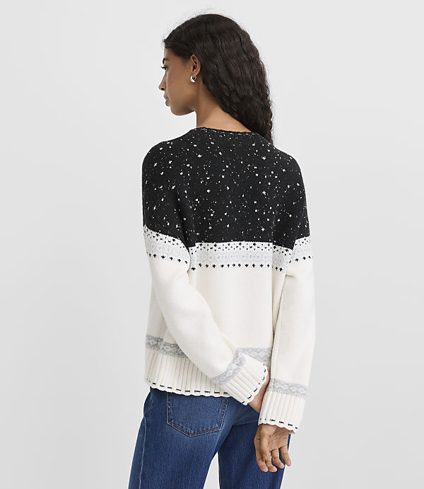 A woman wearing a black and white patterned sweater and blue jeans stands against a plain light gray background.