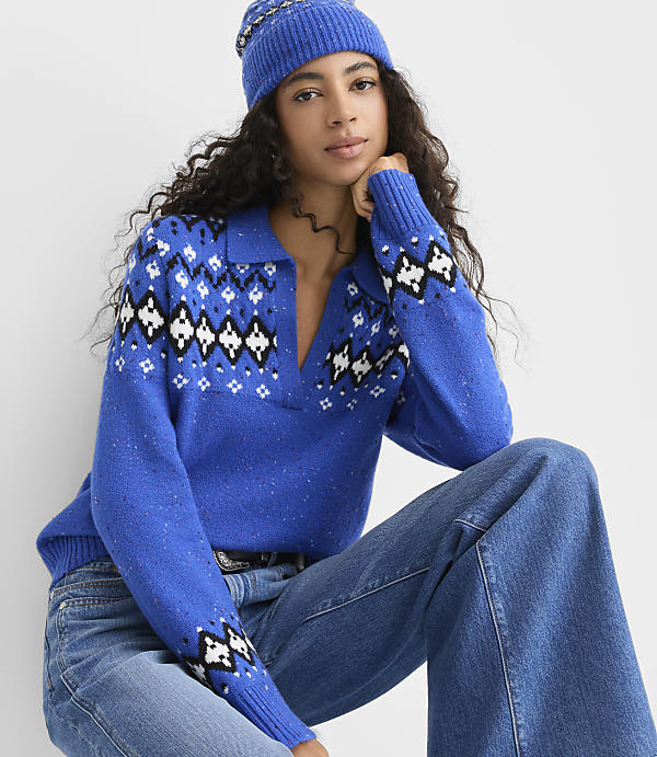 A woman wearing a blue patterned sweater, blue beanie, and jeans poses against a plain white background.