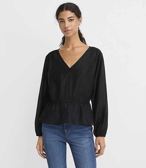 A woman wearing a black long-sleeved blouse and blue jeans stands against a plain white background.