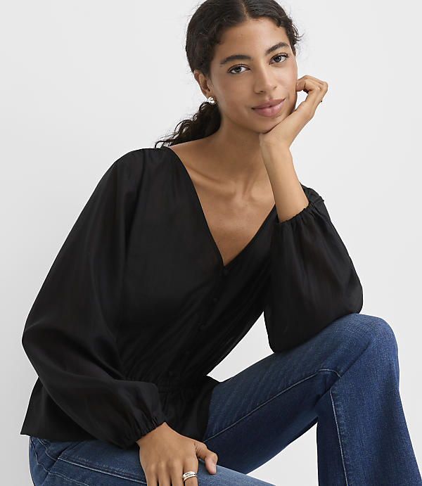A woman wearing a black long-sleeved blouse and blue jeans poses against a plain white background.