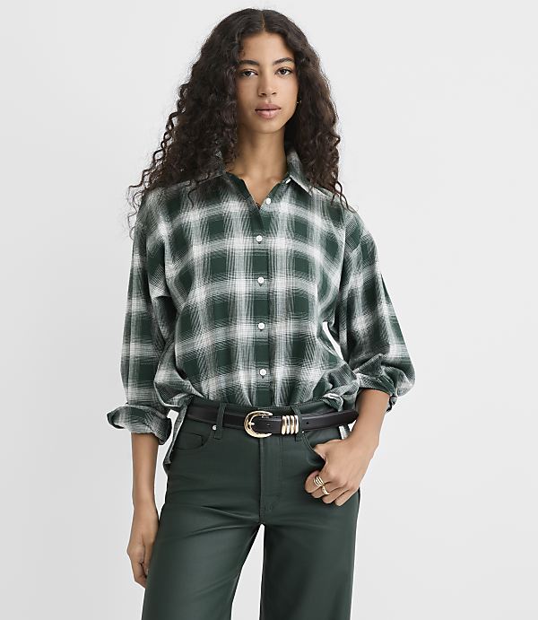 A woman wearing a green plaid shirt and dark green leather pants stands against a plain white background.