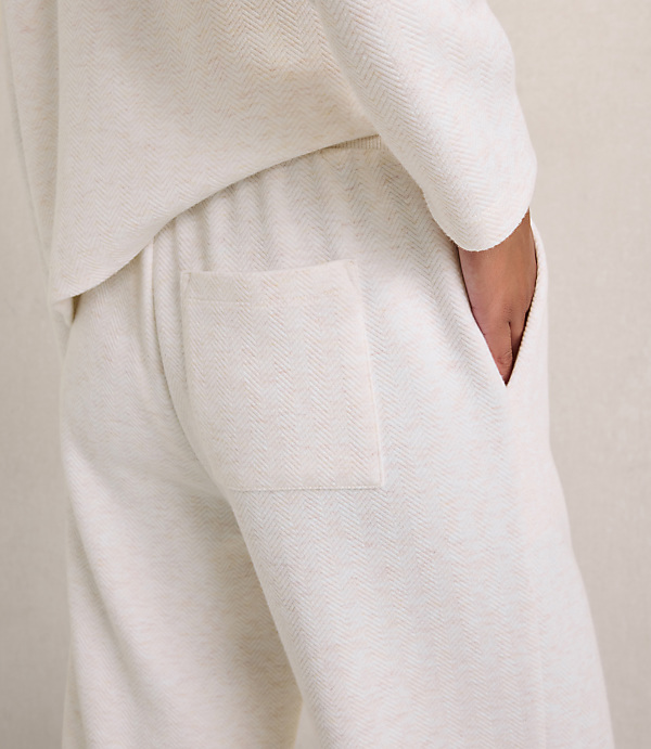A person wears a white textured lounge set with a hand in a pocket against a plain neutral background.