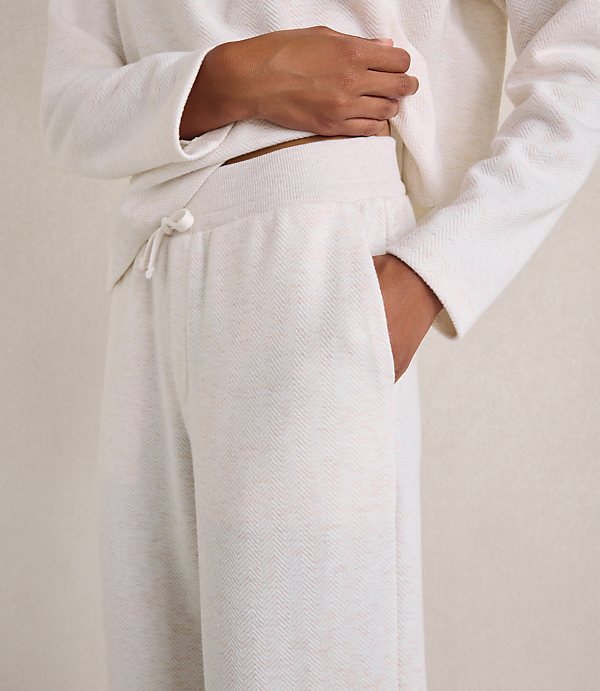 A person wears a white textured lounge set against a plain, neutral-colored wall.