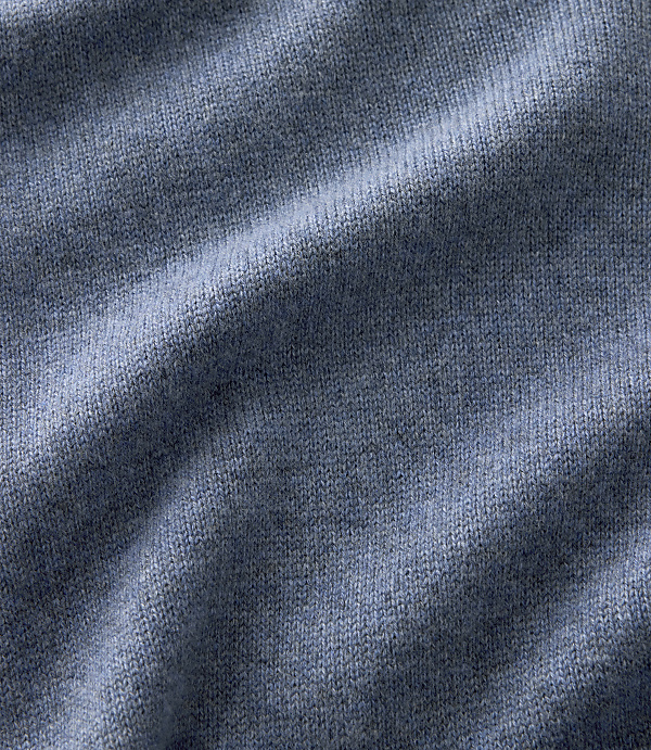 Blue knitted fabric with soft folds in the foreground and a consistent textured weave throughout the background.