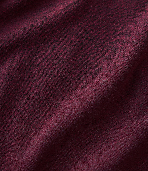 A close-up of maroon fabric with soft folds in the foreground and a slightly blurred texture in the background.
