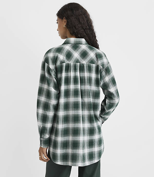 A woman wearing a green and white plaid shirt stands with her back to the camera against a plain white background.