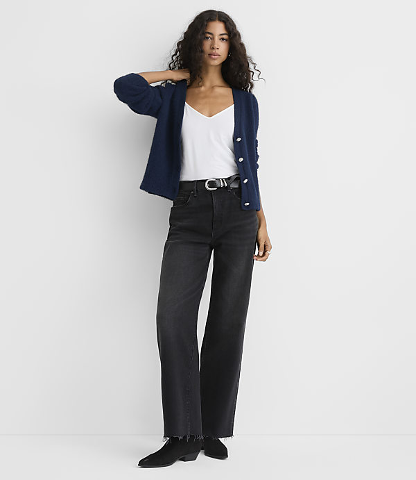 A woman wearing a navy cardigan, white top, and black wide-leg jeans stands against a plain white background.