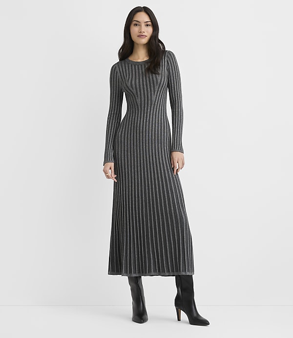 A woman wearing a long-sleeved, ribbed grey maxi dress and black boots stands against a plain white background.