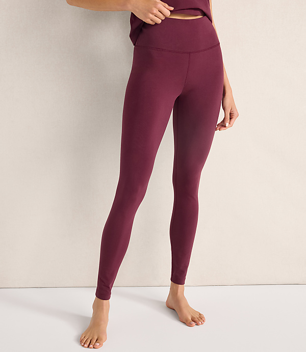 A person wearing maroon leggings stands against a plain, light-colored wall and floor.