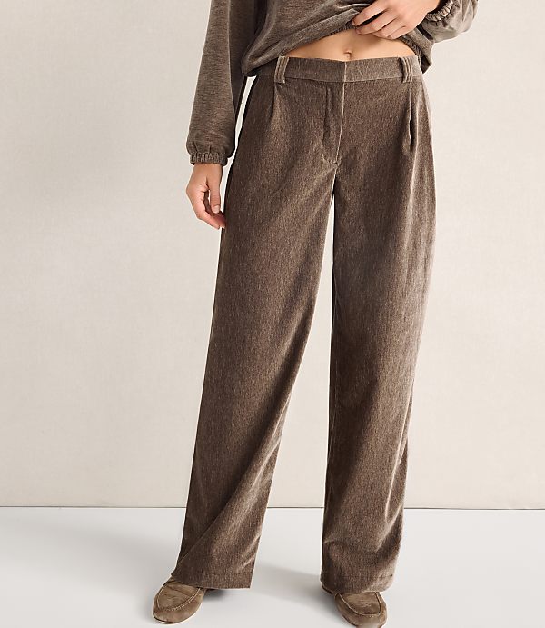 A person wears brown wide-leg trousers and a matching top against a plain, neutral-colored wall.