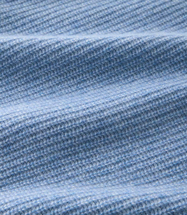 A close-up of light blue ribbed knit fabric with soft folds in the foreground and a blurred texture in the background.