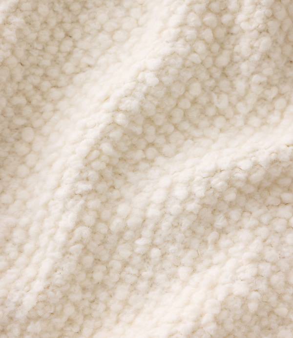 A close-up of soft, cream-colored textured fabric with folds in the foreground and a consistent knit pattern in the background.