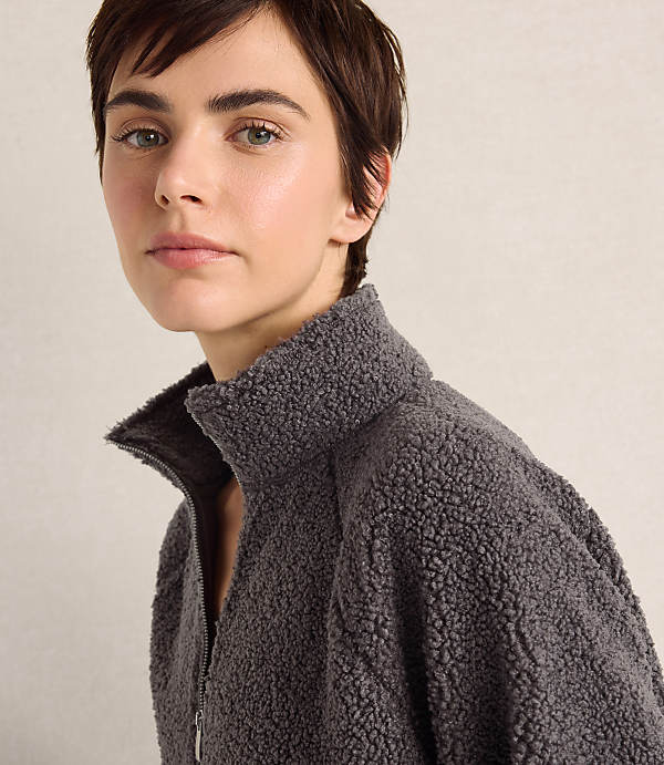 A person with short brown hair wearing a grey fleece jacket stands against a plain, light-colored background.
