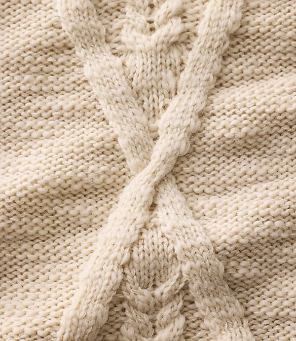 A thick, cream-colored cable knit pattern crosses in the foreground over a textured, knitted background.