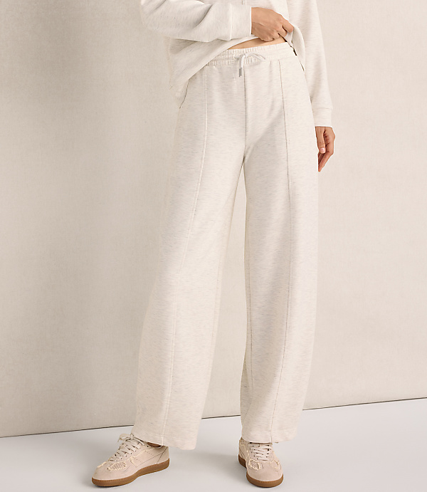 A person wearing a cream-colored sweatshirt and wide-leg lounge pants stands against a neutral, light-beige wall.