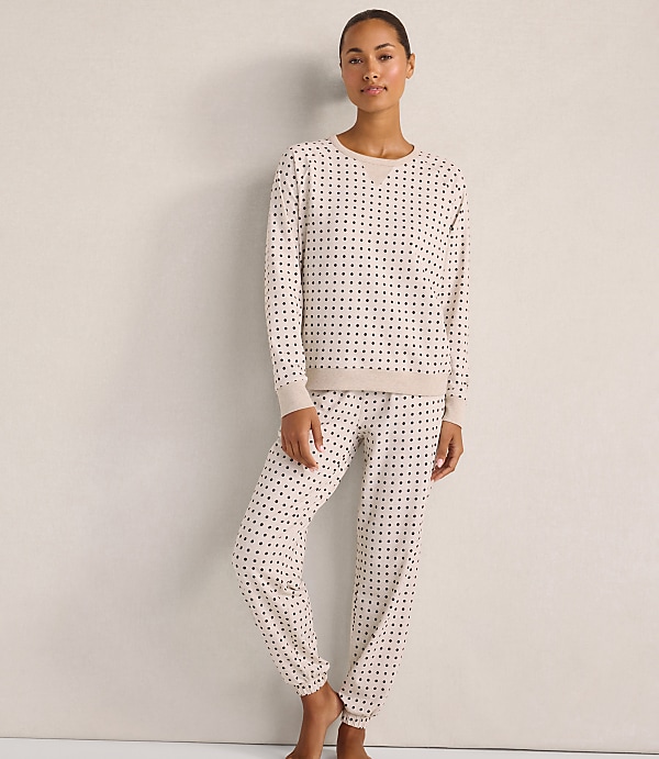 A woman wearing a beige polka-dot pajama set stands against a plain, light-colored wall.