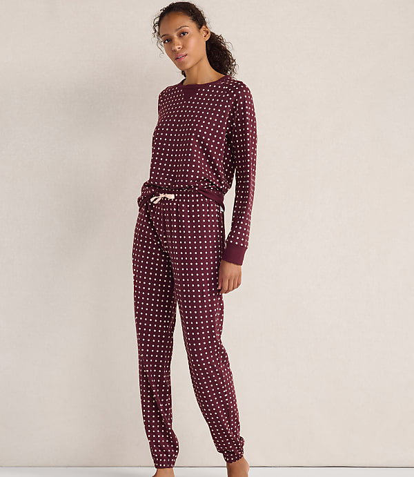 A woman wearing maroon polka-dot pajamas stands against a plain, light-colored wall.