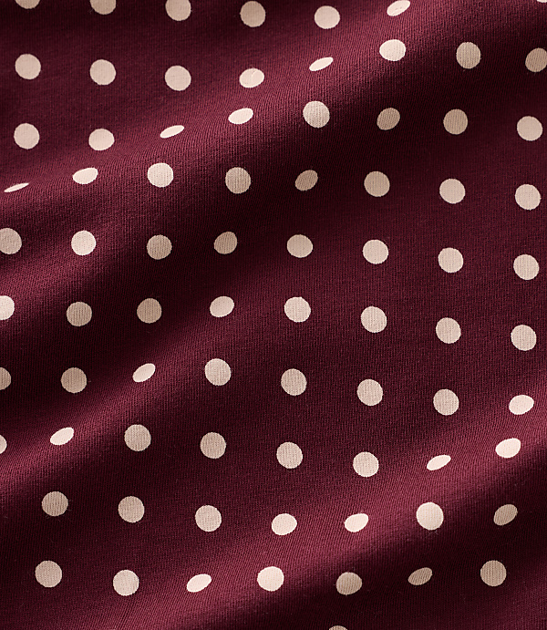 Small white polka dots are scattered across a draped, deep burgundy fabric.