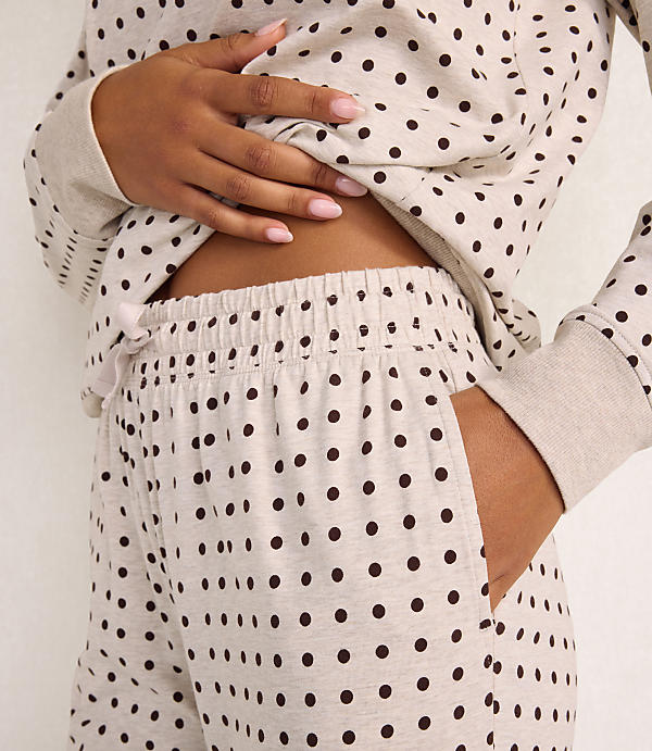 A person wears a beige polka-dot pajama set against a plain white background.