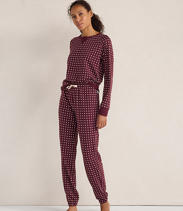A woman wearing maroon polka-dot pajamas stands against a plain, light-colored wall.