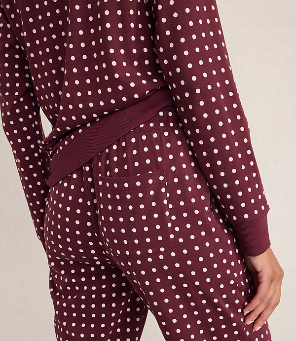 A person wears maroon pajamas with white polka dots against a plain, light-colored background.