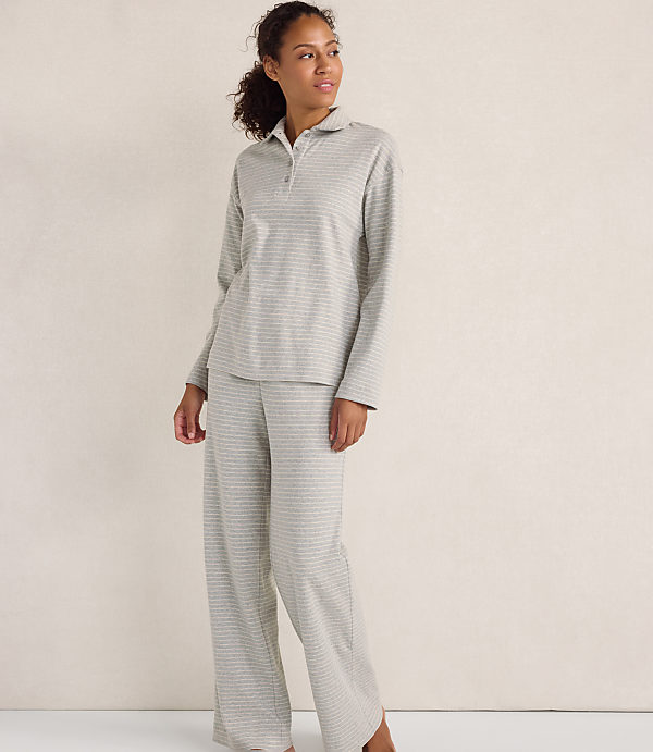 A woman wearing a grey striped pajama set stands against a plain, light-colored wall.