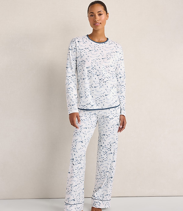 A woman wearing white and blue patterned pajamas stands against a plain, light-colored wall.