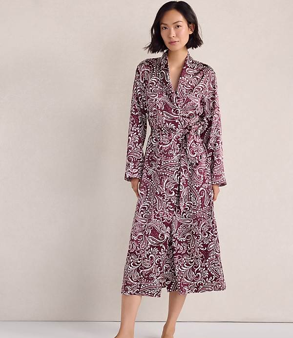 A woman wearing a maroon and white paisley print robe stands against a plain, neutral-colored wall.