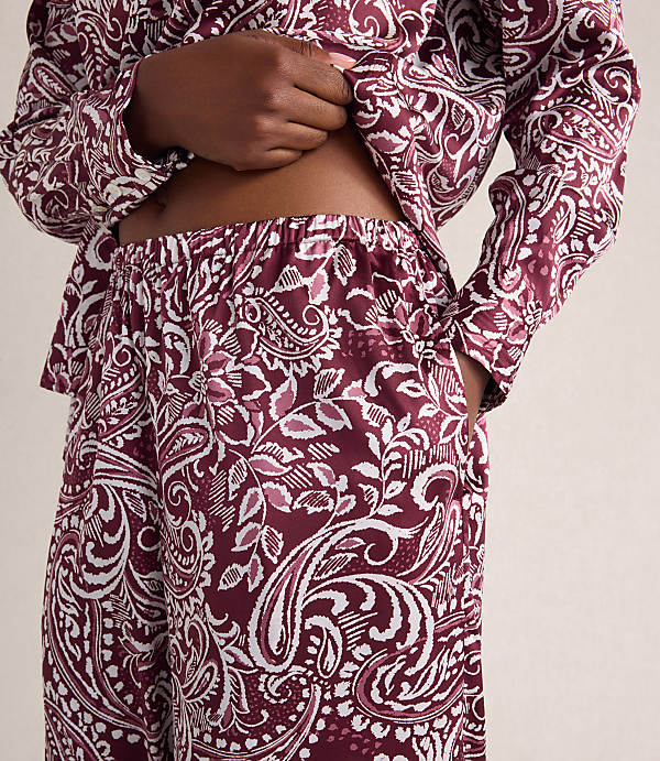 A person wears a maroon and white paisley print pajama set against a plain, light-colored background.