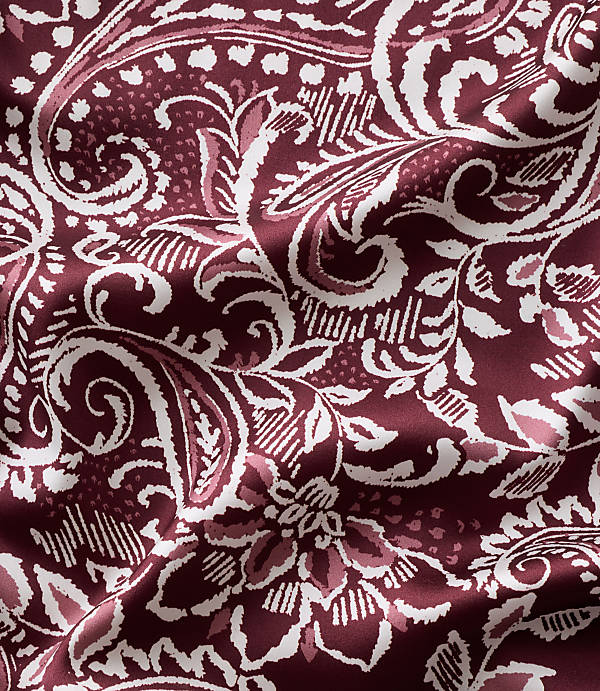 Intricate white and light pink floral and paisley patterns swirl across a deep burgundy fabric with soft folds.
