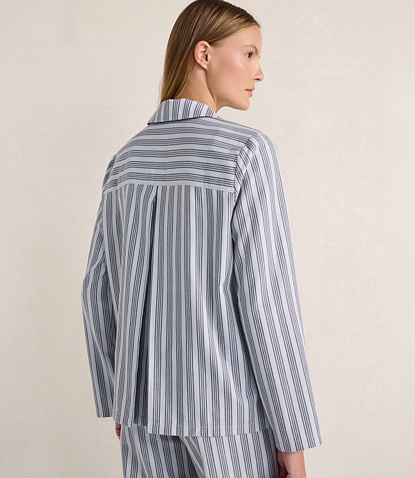 A woman wearing a blue and white striped pajama set stands against a plain, neutral-toned background.