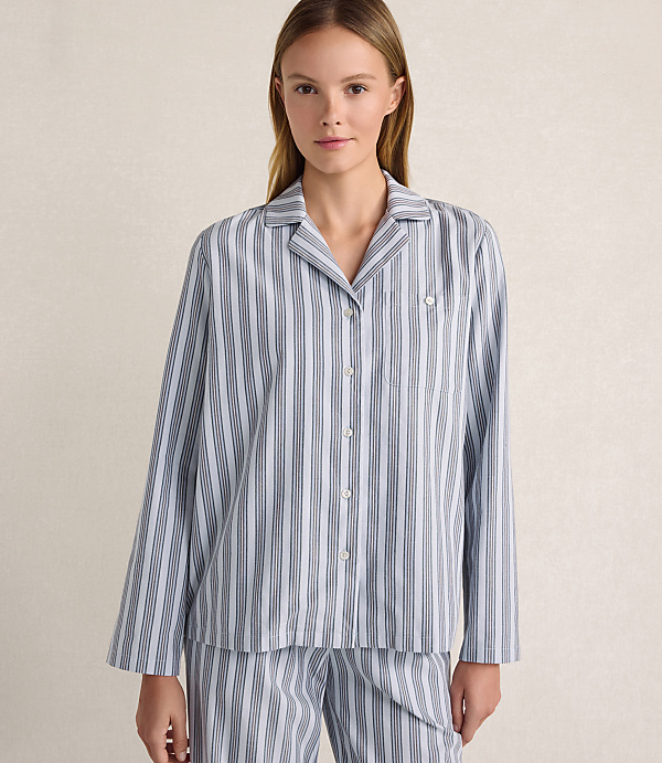 A woman wearing blue and white striped pajamas stands against a plain, light-colored background.