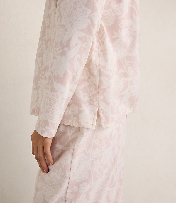 A person wears a light pink and white floral patterned suit against a plain, neutral-toned background.
