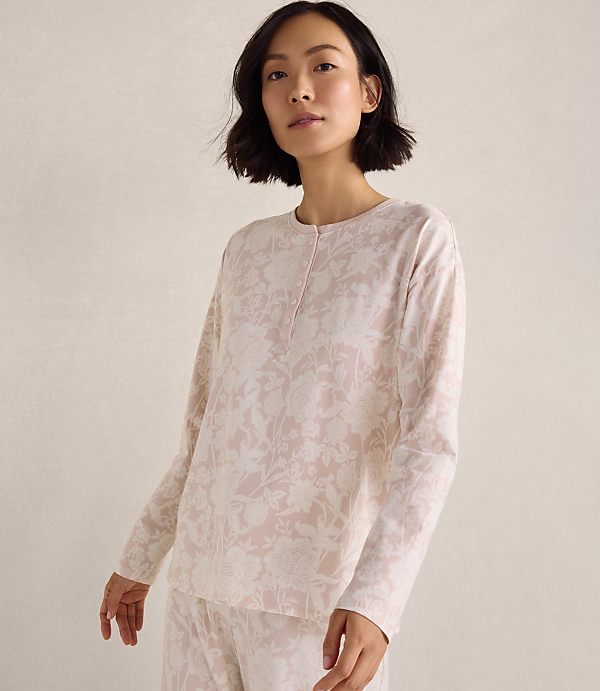 A woman wearing pink floral pajamas stands against a plain, neutral-toned background.