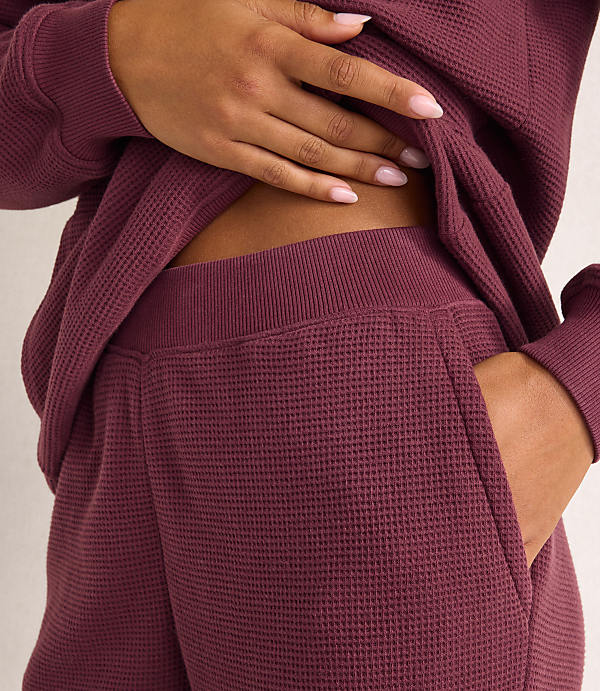 A person's hand rests on their stomach while wearing a maroon waffle-knit lounge set against a plain, light-colored background.