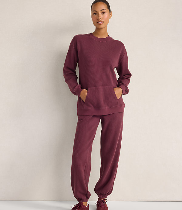 A woman wearing a maroon waffle-knit lounge set stands against a plain, light-colored wall.