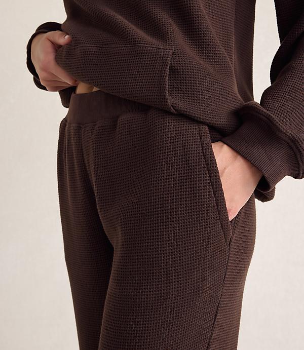 A person wears a brown waffle-knit lounge set against a plain, light-colored background.