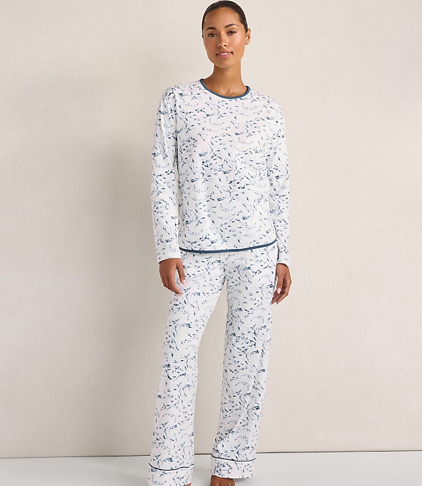 A woman wearing white and blue patterned pajamas stands against a plain, light-colored wall.