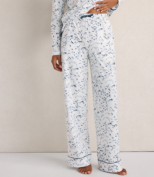 A person wears white pajama pants with a blue marble print against a plain, neutral-colored wall.