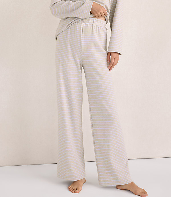 A person wears light-colored, striped lounge pants and a matching top against a plain, neutral-toned wall.