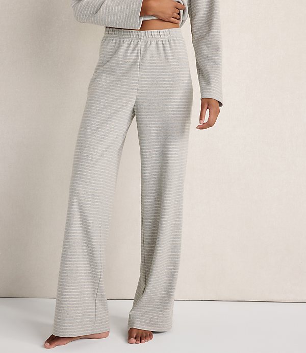 A person wearing grey striped lounge pants and a matching top stands against a plain, light-colored wall.