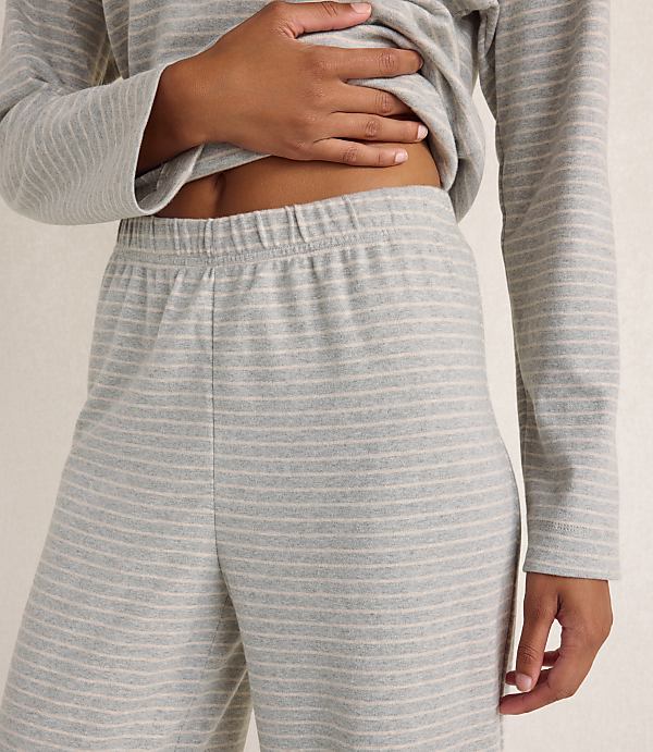 A person wears a grey and white striped lounge set against a plain, neutral-colored wall.