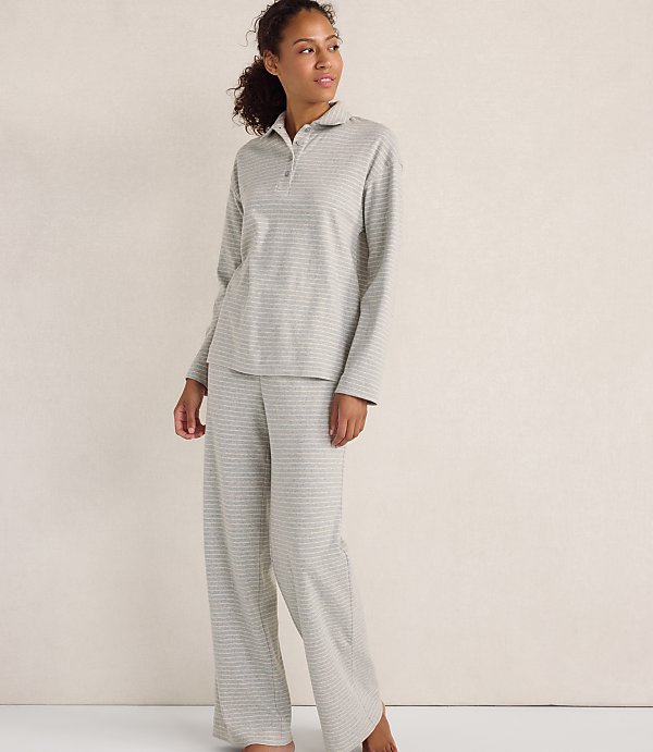 A woman wearing grey striped pajamas stands against a plain, light-colored wall.